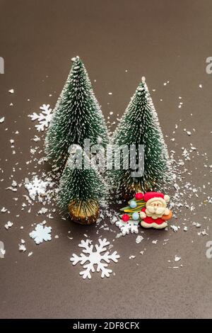 Small decorative Christmas trees with New Year's decor. Santa Claus, snowflakes on black stone concrete background, close up Stock Photo