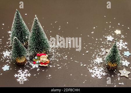 Small decorative Christmas trees with New Year's decor. Santa Claus, snowflakes on black stone concrete background, copy space Stock Photo