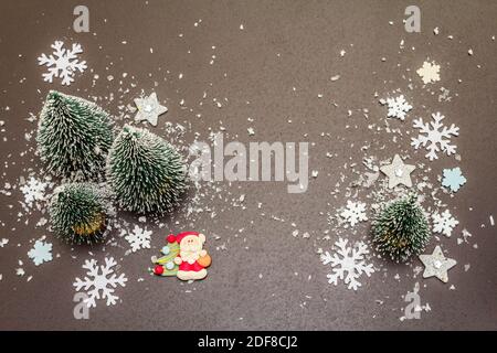 Small decorative Christmas trees with New Year's decor. Santa Claus, snowflakes on black stone concrete background, top view Stock Photo
