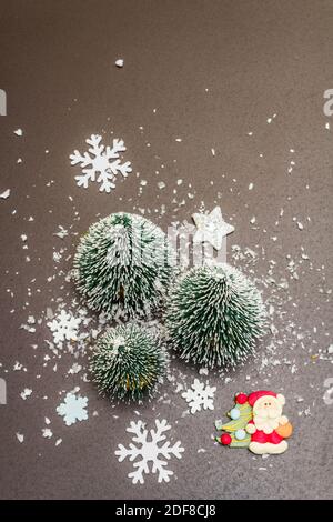 Small decorative Christmas trees with New Year's decor. Santa Claus, snowflakes on black stone concrete background, top view Stock Photo