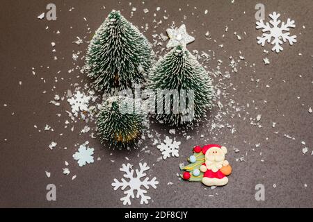 Small decorative Christmas trees with New Year's decor. Santa Claus, snowflakes on black stone concrete background, top view Stock Photo