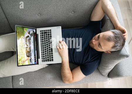 Young Man Lying On Sofa Watching Video On Laptop Stock Photo
