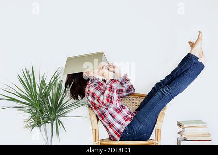 Funny barefoot girl holding a book in front of her face. Lifestyle and school concept. Faceless. Stock Photo