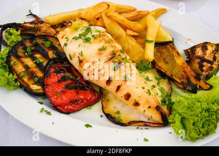 Grilled squid served with vegetables and fries. Traditional Greek dish. Stock Photo