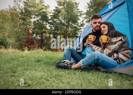 Romantic couple sitting near tent with cups of hot tea in their hands Stock Photo