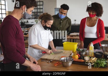 Female chef and divserse group wearing face masks in kitchen Stock Photo