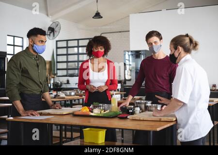 Female chef and divserse group wearing face masks in kitchen Stock Photo