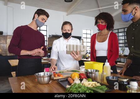 Female chef and divserse group wearing face masks in kitchen Stock Photo