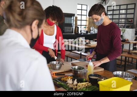 Female chef and divserse group wearing face masks in kitchen Stock Photo