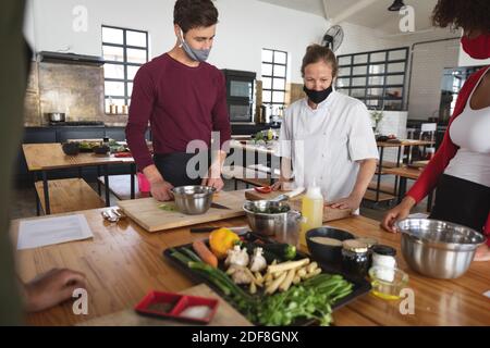 Female chef and divserse group wearing face masks in kitchen Stock Photo