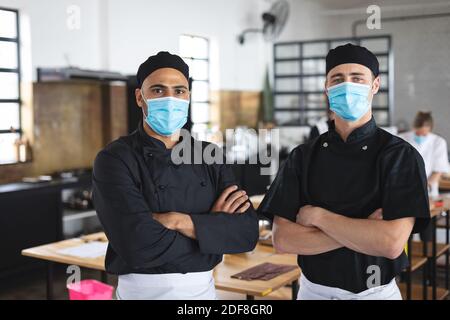 Two divserse male chefs wearing face masks in kitchen Stock Photo
