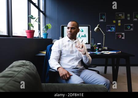 Mixed race businessman sitting by desk in office, thinking Stock Photo