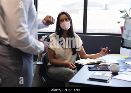 Mixed race businesswoman wearing face mask working in office Stock Photo
