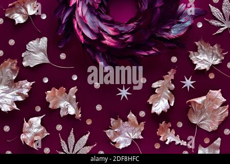 Autumn leaves with metallic golden paint, feather wreath on dark burgundy linen textile background. Stock Photo