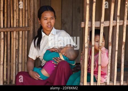 A woman of the AKHA tribe nurses a child in her bamboo house -  village near KENGTUNG or KYAINGTONG - MYANMAR Stock Photo