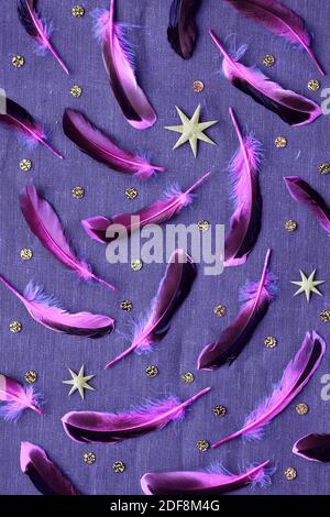 Scattered pink purple feathers. Canvas linen background with the feathers, gold stars and confetti. Stock Photo