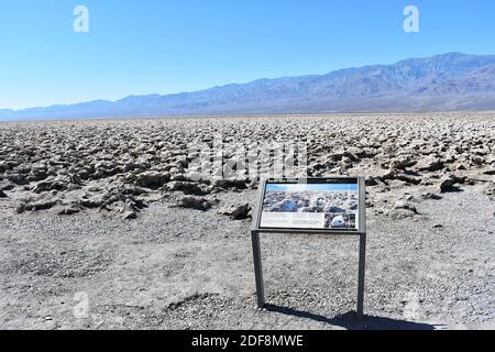 Devils Golf Course with the Armargosa Mountain Range behind in Death Valley National Park. A sign for visitors stands by the salt crystal formations. Stock Photo