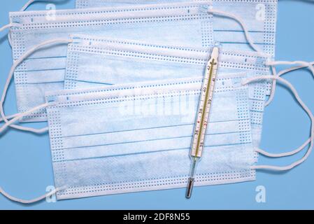 Medical surgical protective face masks and glass thermometer for measuring the temperature of the human body on light blue background. Stock Photo