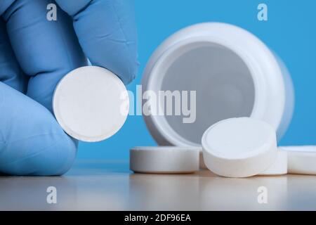 Hand in medical gloves holds big white pill near empty bottle of tablets. Stock Photo