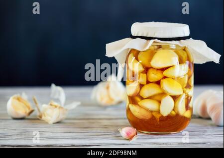 Fermented garlic cloves in a jar of honey, a rich source of probiotics, over a rustic wood background table. Selective focus with blurred background a Stock Photo