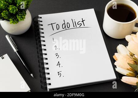 To do list. Notebook and coffee cup on black background. Stock Photo