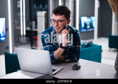 View of concentrated talented skilled male focused on screen of laptop computer, reads necessary information for creating budget report. Stock Photo