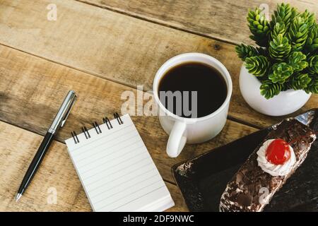 Small spiral notepad butterscotch cake and coffee on rustic wood. Stock Photo