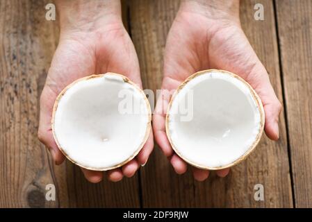 cut half coconut in hand and fresh coconuts on old wooden table for food Stock Photo