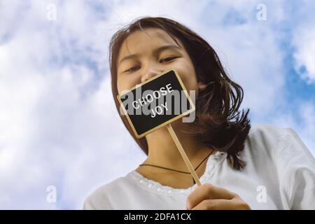 Happy asian teenage girl holding a wooden sign stick written with the word choose joy. Stock Photo