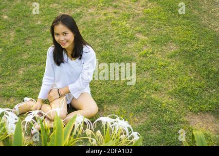 Happy smiling young Asian teenage girl sitting on grass in the park. Stock Photo