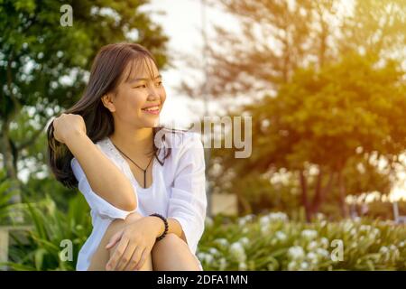 Happy smiling young Asian teenage girl sitting and flipping her hair. Stock Photo