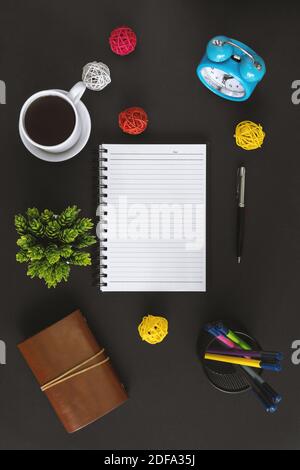 Notepad, coffee and alarm clock on black background. Office table still life. Stock Photo