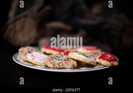 Fresh, homemade Christmas cookies set out for Santa. Sugar cookies with sprinkles and icing by the fireplace and the Christmas tree. Time to decorate Stock Photo