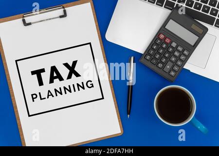 Tax Planning on Paper. Top View of Laptop, Calculator and Coffee Cup on Blue Office Desk. Business concept. Stock Photo