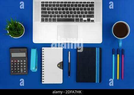 Office desk working space. Laptop, notebook, calculator and coffee on blue background. Business concept. Stock Photo