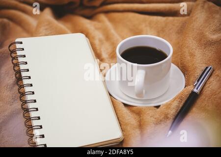 Selective focus view of notebook, pen and coffee cup on blanket. Stock Photo