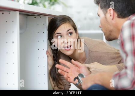 woman looking at male plumber cleaning clogged pipes Stock Photo