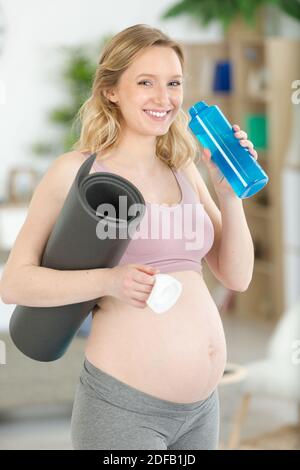 pregnant woman holding rolled up exercise mat drinking water Stock Photo