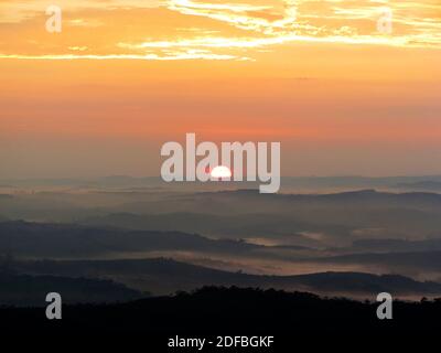 Golden and orange sunrise iluminating a forest. Montains, forests, hills are showed in lays in the picture Stock Photo