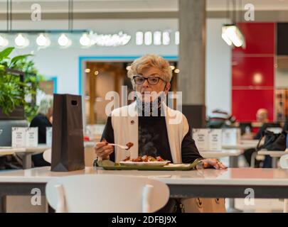 A senior woman with protective mask sitting in the cafeteria and having her breakfast. Selective focus, street view. Langley, BC, Canada-November 9, 2 Stock Photo
