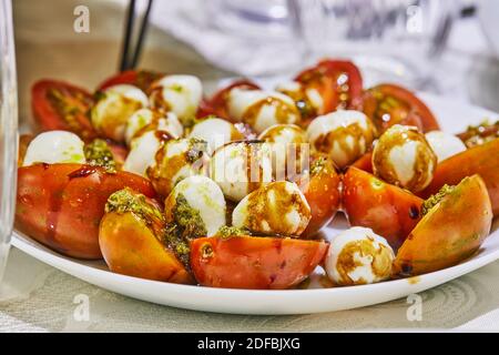 Sliced tomato salad and baby mozzarella on a plate on a served table. Healthy eating Stock Photo