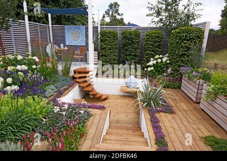 A COLOURFUL SHOW GARDEN WITH SEATING AND DECKING FOR AN URBAN GARDEN. Planting around the raised covered seating area with decking  and a sunken area Stock Photo