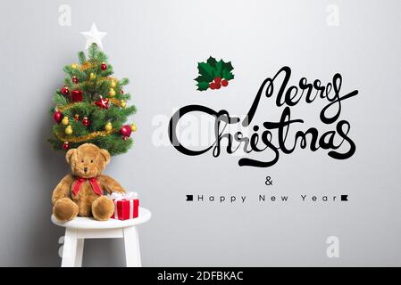 Gift boxes,teddy bear and small decorated Christmas tree on the chair with MERRY CHRISTMAS and HAPPY NEW YEAR 2017 text on the wall Stock Photo