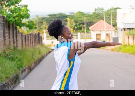 african woman exercising outdoor, listening to music while stretching her arm Stock Photo