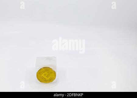 Slowly melting ice cube with a bitcoin token frozen in it on white background with copy space. Concept of frozen assets, frozen economy, cold money or Stock Photo