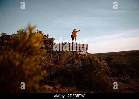 Low angle view of young man pointing at something with woman standing on peak of cliff Stock Photo