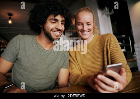 Portrait of happy couple using smartphone and smiling while sitting and relaxing in cafe Stock Photo