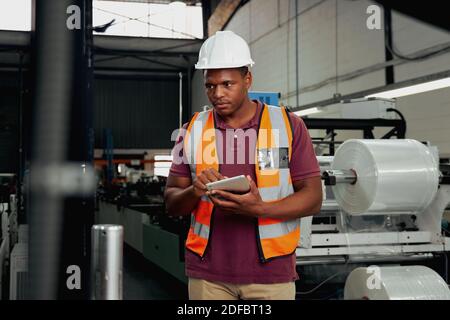Expert male worker in uniform working in a modern factory using digital tablet to check on machinery - latest technology in factory Stock Photo