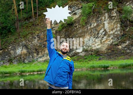 young smiling man holds white sign in blur nature background Stock Photo