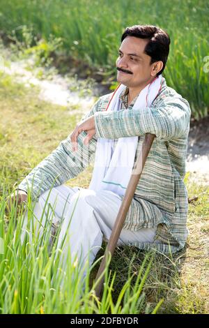 Indian farmer sitting in the field with a shovel, sluggish after ...